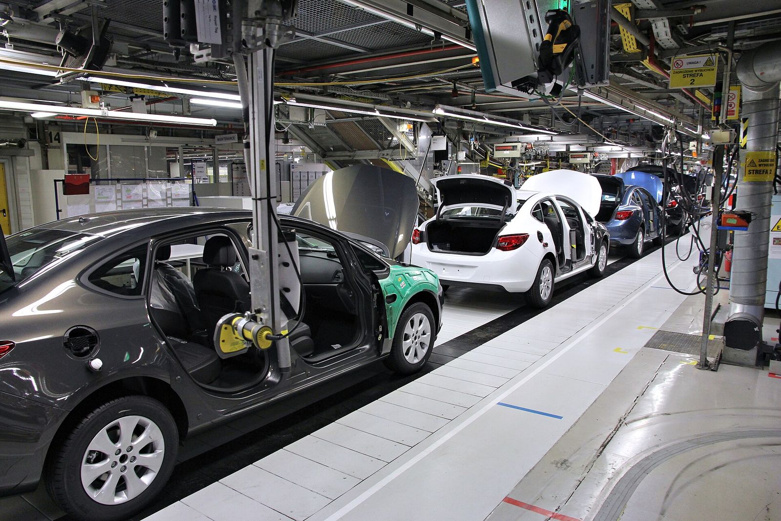 A production line inside a factory, with part-built units moving along it between overhead services.