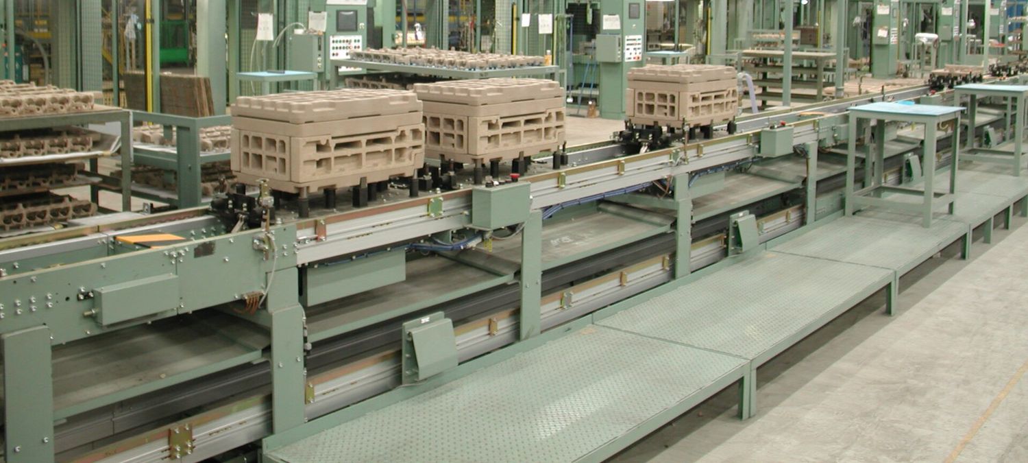 A line of industrial machines installed in a plant, linked by a conveyor carrying parts between them.